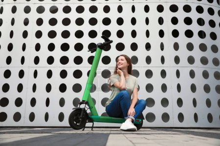Photo for Happy woman sitting on modern electric kick scooter on city street - Royalty Free Image