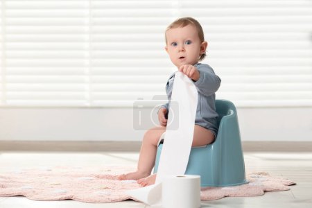 Little child with toilet paper roll sitting on plastic baby potty indoors. Space for text