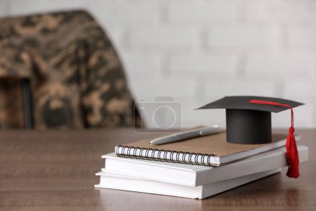 Notebooks, mortarboard and pen on wooden table, space for text. Military education