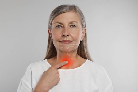 Téléchargez les photos : Système endocrinien. Femme âgée faisant l'auto-examen thyroïdien sur fond gris clair - en image libre de droit
