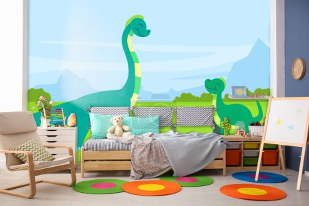 Foto de Interior de la habitación del niño con cama cómoda y otros muebles. Fondos de pantalla de estilo de dibujos animados con dinosaurios - Imagen libre de derechos
