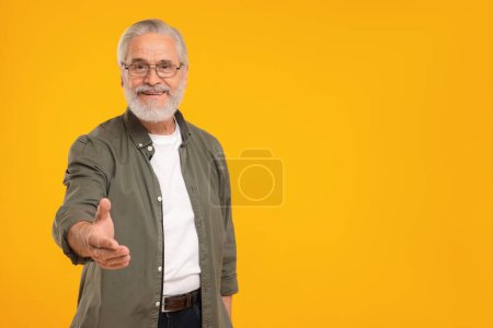 Téléchargez les photos : Senior en lunettes accueillant et offrant poignée de main sur fond jaune, espace pour le texte - en image libre de droit