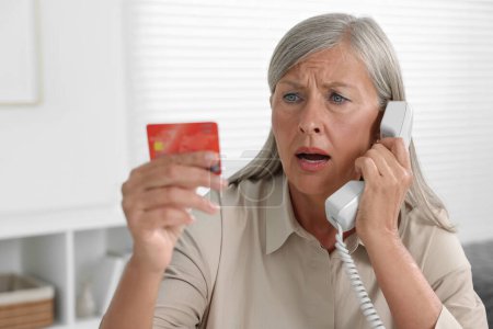 Worried woman with credit card talking on phone indoors. Be careful - fraud