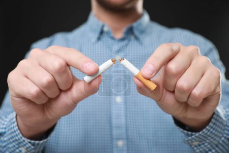 Rauchstopp-Konzept. Mann mit zerbrochenen Zigarettenstücken auf schwarzem Hintergrund, Nahaufnahme