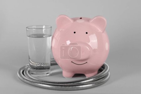 Water scarcity concept. Piggy bank, shower hose and glass of drink on grey background