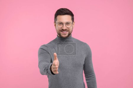 Téléchargez les photos : Homme heureux accueillant et offrant poignée de main sur fond rose - en image libre de droit