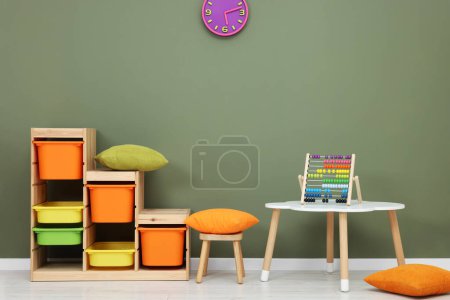 Foto de Mesa con silla, estantes y abacus juguete cerca de la pared de olivo en la sala de juegos. Interior de jardín de infantes con estilo - Imagen libre de derechos