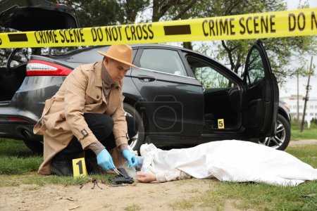 Foto de Investigador en guantes protectores trabajando en la escena del crimen con cadáver al aire libre - Imagen libre de derechos