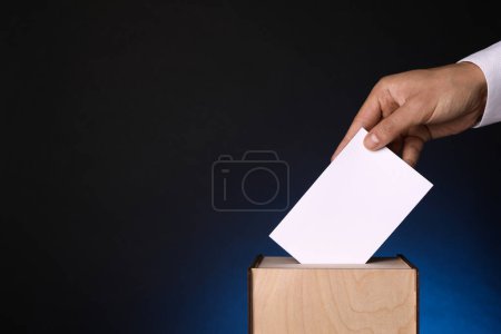 Foto de Hombre poniendo su voto en urnas sobre fondo azul oscuro, primer plano. Espacio para texto - Imagen libre de derechos