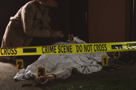 Foto de Investigador examinando la escena del crimen con el cuerpo muerto al aire libre, se centran en cinta amarilla - Imagen libre de derechos