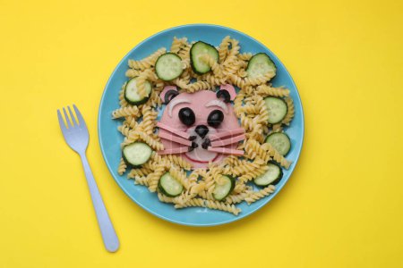 Téléchargez les photos : Service créatif pour les enfants. Assiette avec ours mignon faite de pâtes savoureuses, légumes et saucisses sur fond jaune, plat - en image libre de droit