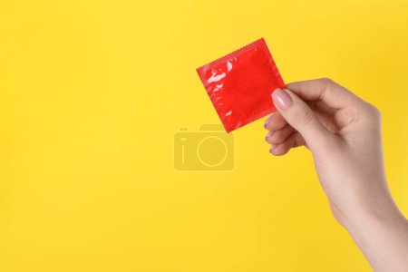 Femme tenant un préservatif sur fond jaune, gros plan. Espace pour le texte