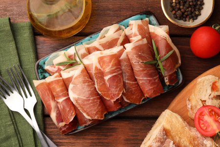 Photo for Rolled slices of delicious jamon served with different products on wooden table, flat lay - Royalty Free Image