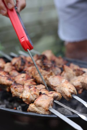 Photo for Man measuring temperature of delicious kebab on metal brazier outdoors, closeup - Royalty Free Image