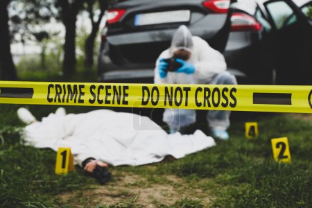 Foto de Criminólogo tomando fotos de cadáver en la escena del crimen al aire libre, se centran en cinta amarilla - Imagen libre de derechos