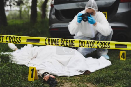 Foto de Criminólogo tomando fotos de cadáver en la escena del crimen al aire libre, se centran en cinta amarilla - Imagen libre de derechos