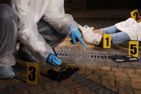 Foto de Criminólogo en guantes de protección trabajando en la escena del crimen con el cuerpo muerto al aire libre, primer plano - Imagen libre de derechos