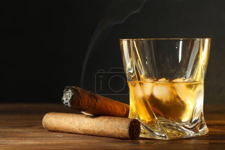 Foto de Vaso de whisky con cubitos de hielo y cigarros en la mesa de madera, primer plano - Imagen libre de derechos