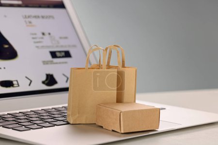 Foto de Mini bolsas de compras y caja en el ordenador portátil contra fondo gris claro, primer plano. Tienda online - Imagen libre de derechos