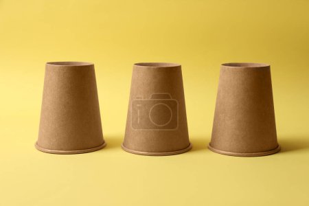 Téléchargez les photos : Trois tasses en papier sur fond jaune. Jeu de Thimblerig - en image libre de droit