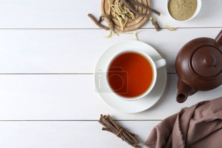 Aromatic licorice tea in cup, dried sticks of licorice root and powder on white wooden table, flat lay. Space for text