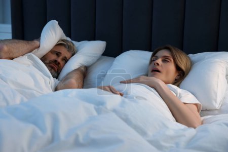 Téléchargez les photos : Un homme irrité se couvrant les oreilles avec des oreillers dans son lit à la maison. Problème avec ronflement femme - en image libre de droit