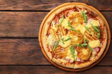 Delicious pineapple pizza with arugula on wooden table, top view. Space for text
