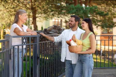 Freundliches Verhältnis zu den Nachbarn. Junges Paar mit Weidenkorb behandelt Seniorin nahe Zaun im Freien