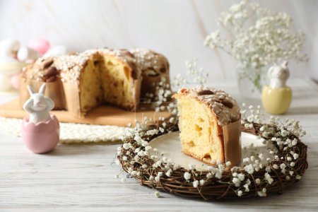 Delicious Italian Easter dove cake (traditional Colomba di Pasqua) in nest and festive decor on white wooden table, space for text