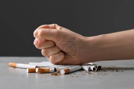 Photo for Stop smoking concept. Woman crushing cigarettes at gray table, closeup - Royalty Free Image