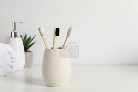Téléchargez les photos : Brosses à dents en bambou dans le support, plante en pot, serviette et produit cosmétique sur comptoir blanc, espace pour le texte - en image libre de droit