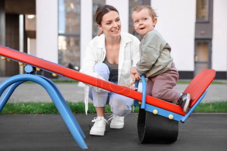 Photo for Happy nanny and cute little boy on seesaw outdoors - Royalty Free Image