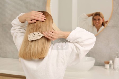 Schöne Frau beim Haare putzen in der Nähe von Spiegel im Badezimmer