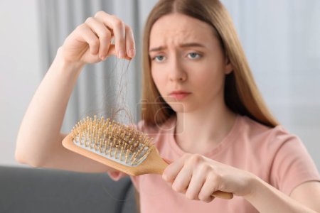 Woman untangling her lost hair from brush at home, selective focus. Alopecia problem