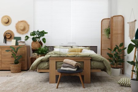 Téléchargez les photos : Chambre élégante avec lit confortable et belles plantes d'intérieur vertes. Design d'intérieur - en image libre de droit
