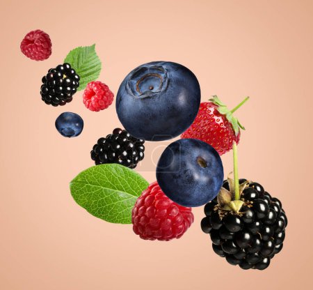 Many different fresh berries falling on pink beige background