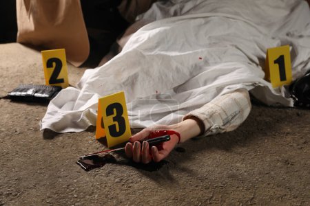 Foto de Escena del crimen con cuerpo de mujer muerta, cuchillo ensangrentado y marcadores al aire libre, primer plano - Imagen libre de derechos