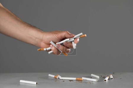 Foto de Deja de fumar concepto. Hombre sosteniendo cigarrillos sobre la mesa gris, primer plano - Imagen libre de derechos