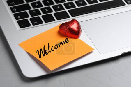 Téléchargez les photos : Note collante avec mot Bienvenue et bonbons sur ordinateur portable, gros plan - en image libre de droit
