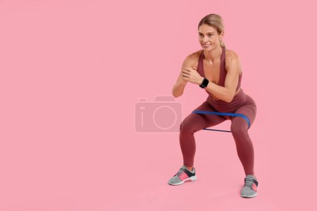 Mujer ejercitándose con banda de resistencia elástica sobre fondo rosa. Espacio para texto
