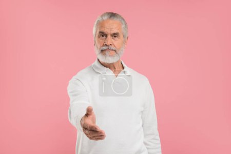 Téléchargez les photos : Senior homme accueillant et offrant poignée de main sur fond rose - en image libre de droit