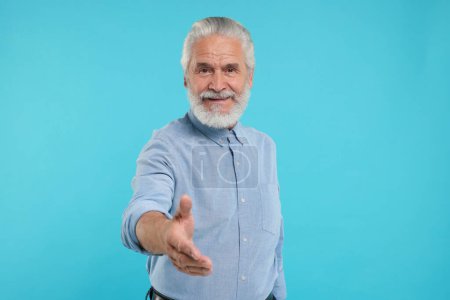 Téléchargez les photos : Senior homme accueillant et offrant poignée de main sur fond bleu clair - en image libre de droit