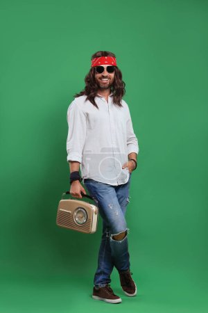 Foto de Elegante hombre hippie en gafas de sol con receptor de radio retro sobre fondo verde - Imagen libre de derechos