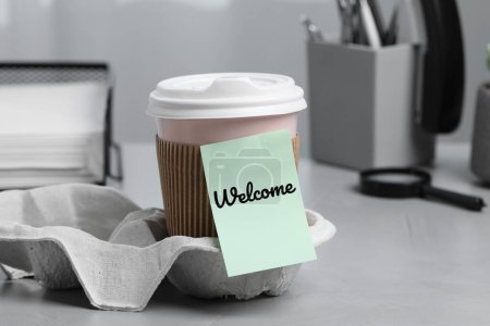 Téléchargez les photos : Note collante avec mot Bienvenue attaché à la tasse de café en papier sur le bureau - en image libre de droit