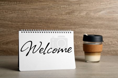 Téléchargez les photos : Carnet avec mot Bienvenue et tasse de café sur la table - en image libre de droit