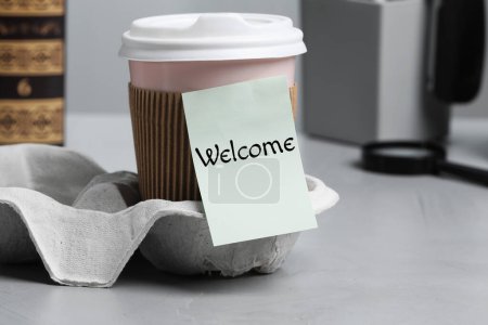 Téléchargez les photos : Note collante avec mot Bienvenue attaché à la tasse de café en papier sur le bureau - en image libre de droit
