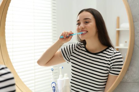 Foto de Mujer joven cepillándose los dientes con cepillo de dientes de plástico cerca del espejo en el baño - Imagen libre de derechos