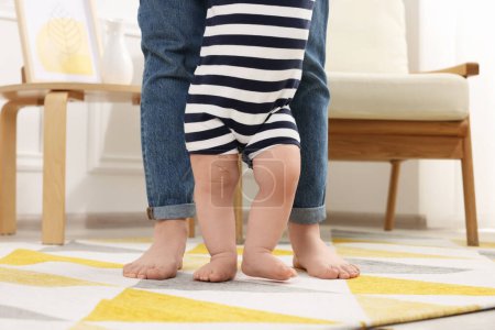 Mutter unterstützt ihren kleinen Sohn, während er zu Hause lernt, auf Teppich zu gehen, Nahaufnahme