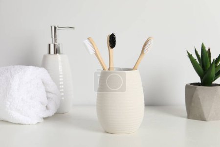 Téléchargez les photos : Brosses à dents en bambou dans le support, plante en pot, serviette et produit cosmétique sur comptoir blanc - en image libre de droit