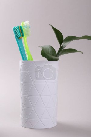 Téléchargez les photos : Brosses à dents et brindilles en plastique coloré dans un récipient sur fond clair - en image libre de droit